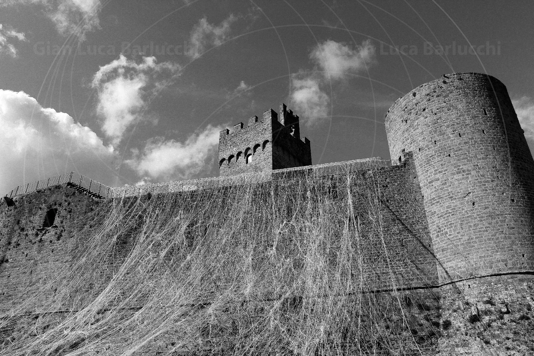 Black-and-white view of stone fortress walls and a round tower at Staggia Senese