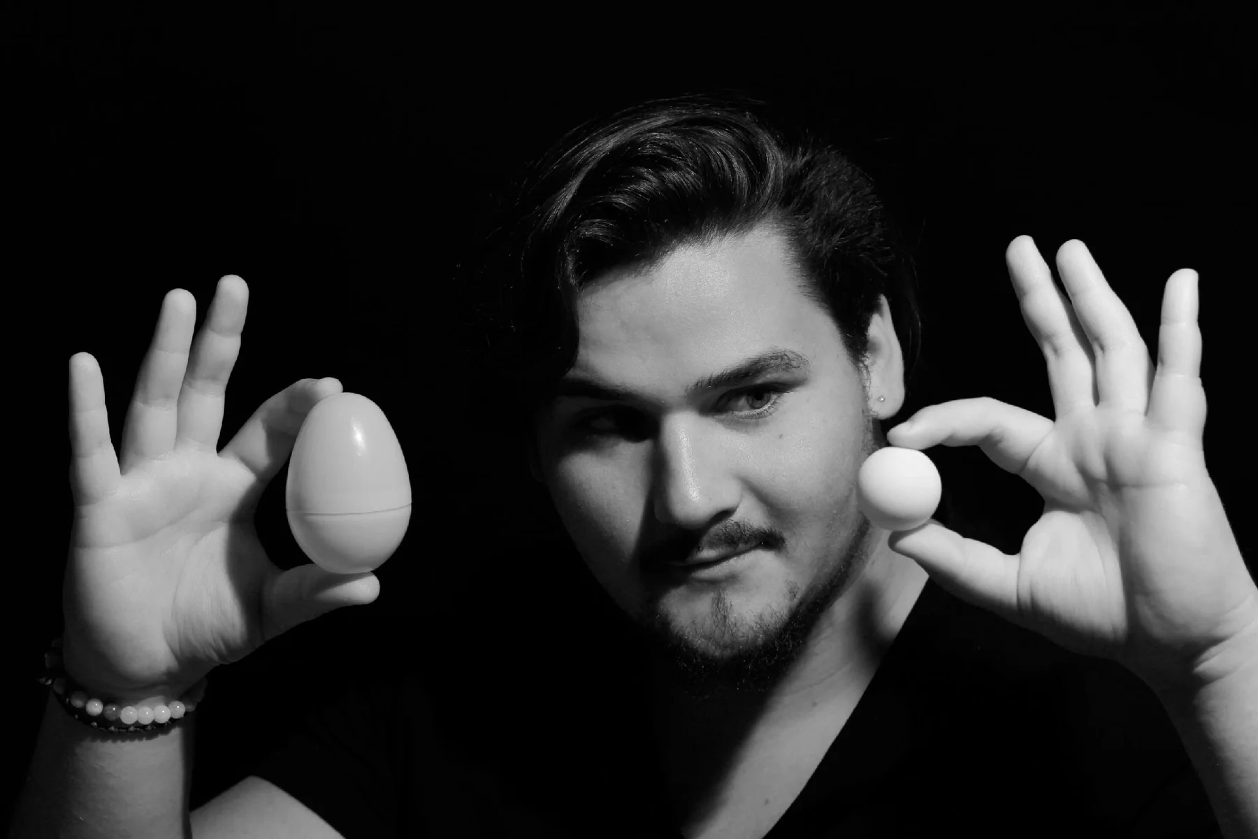 Black-and-white portrait of a young man holding two egg-shaped objects