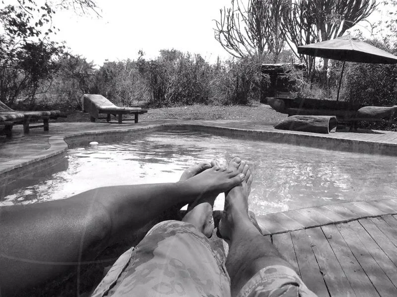 Black-and-white view of a person's outstretched legs beside a swimming pool