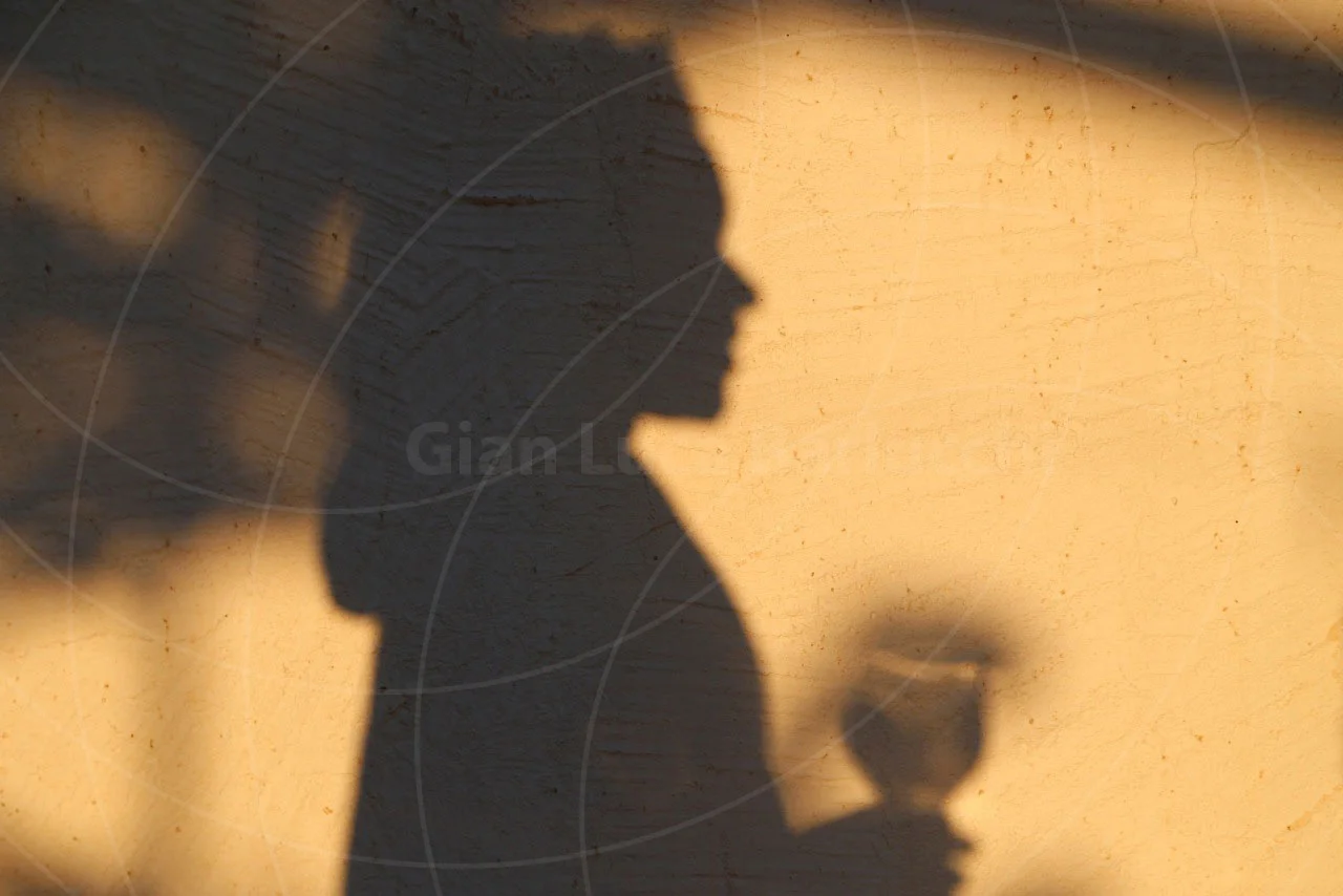 Shadow of a person holding a glass cast on a warm-toned wall