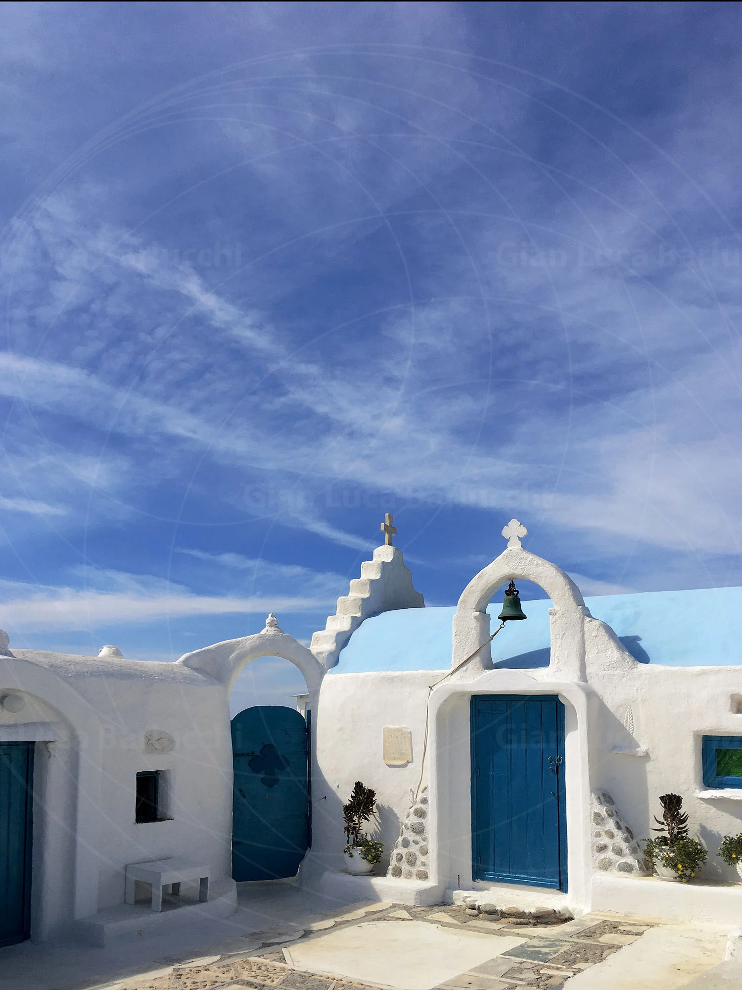 Whitewashed Mykonos church with blue doors and a curved bell gable
