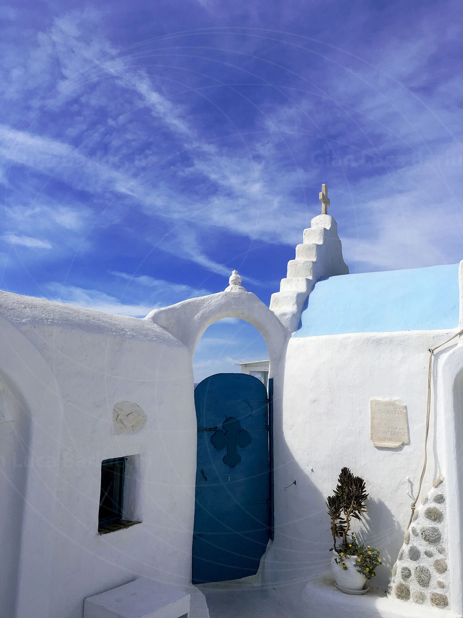 Whitewashed Mykonos church with a blue door beneath a wispy sky