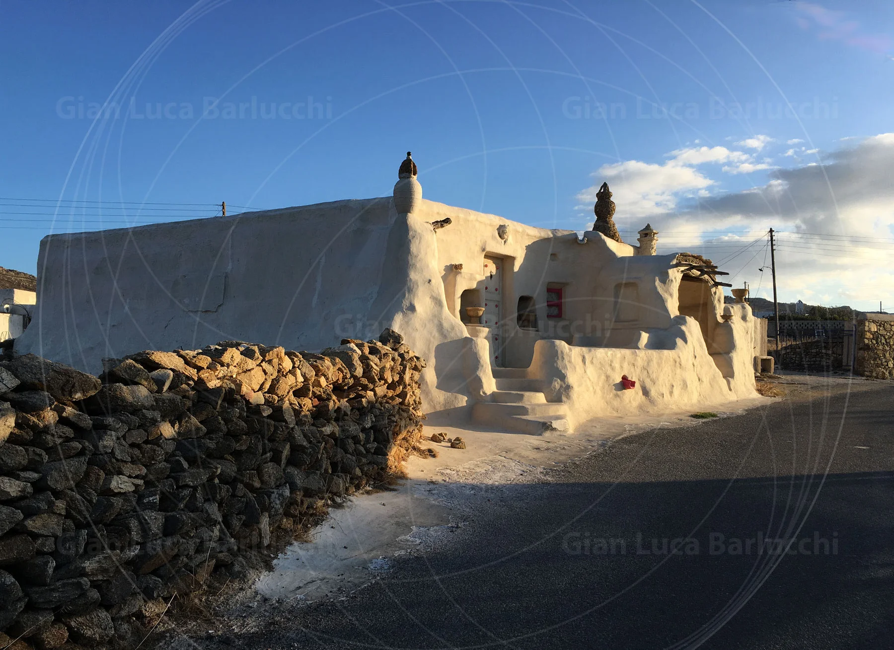Low whitewashed building beside a stone wall and road on Mykonos
