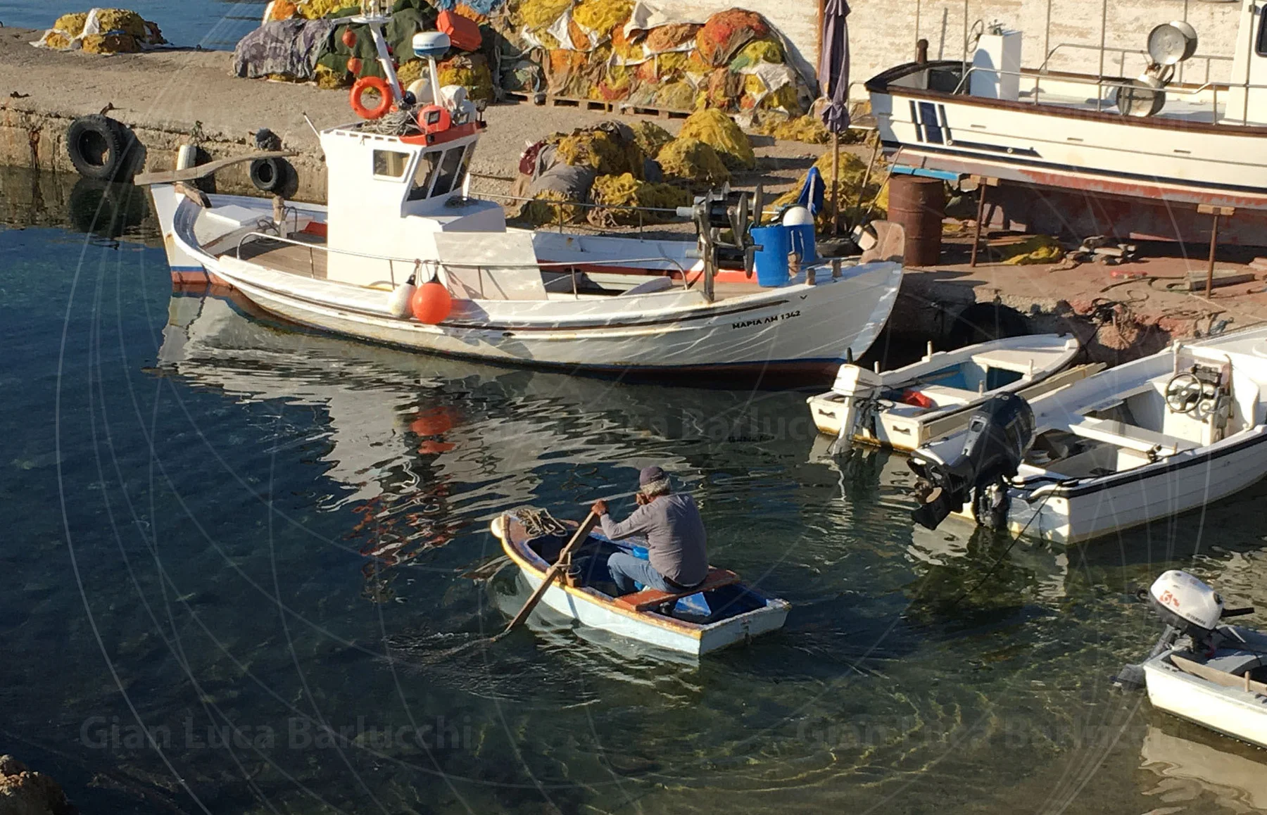 Small boats moored in clear water beside a working harbour on Mykonos