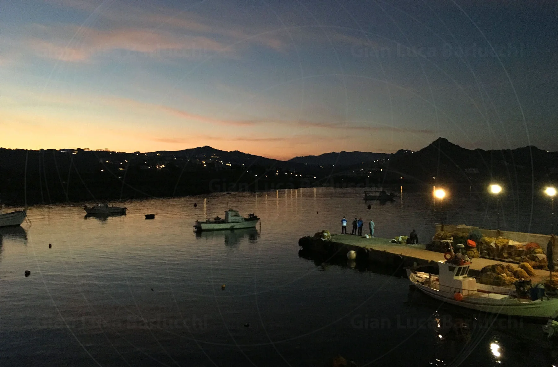 Boats resting in a Mykonos harbour beneath a fading sunset