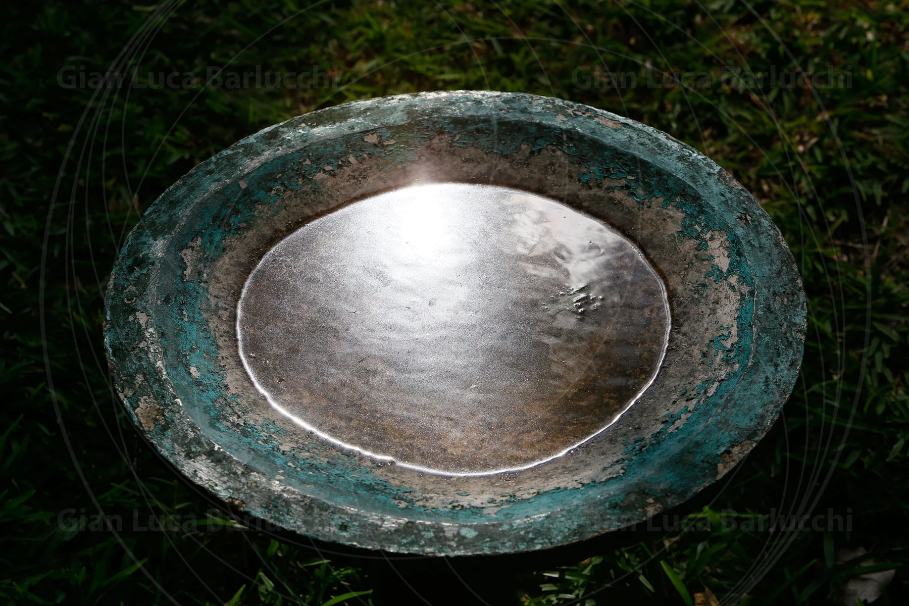 Sky reflected in a round metal basin set on a weathered green stand