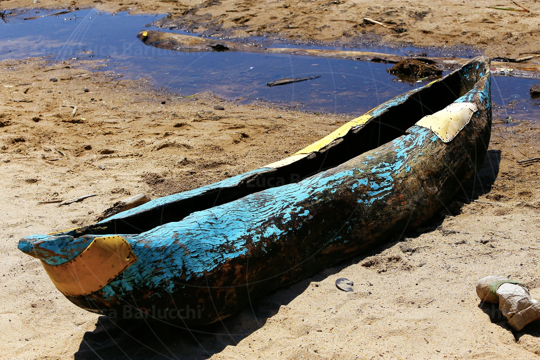 Peeling blue paint on a wooden canoe beside shallow water