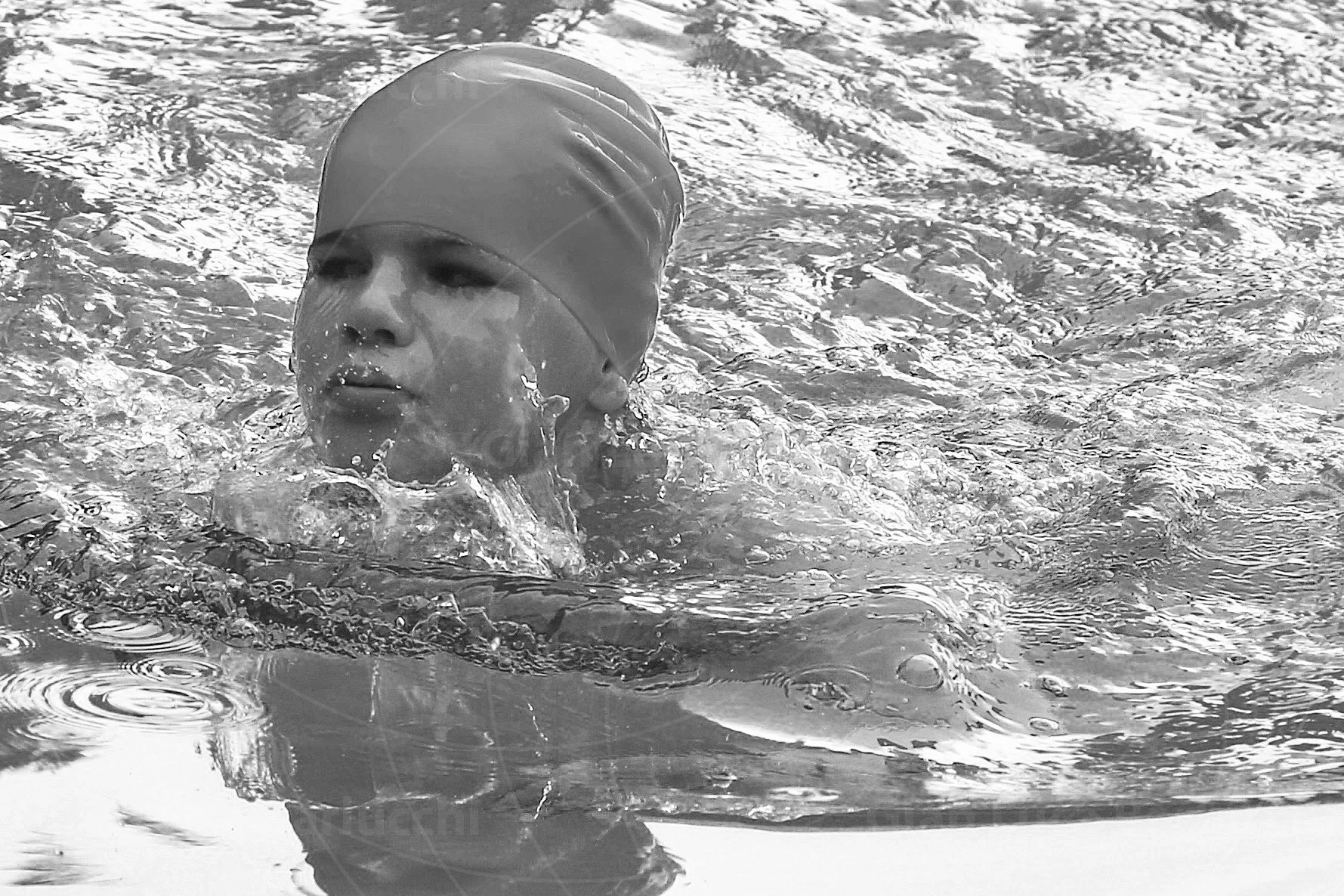 Black-and-white photograph of a swimmer wearing a cap in rippling water