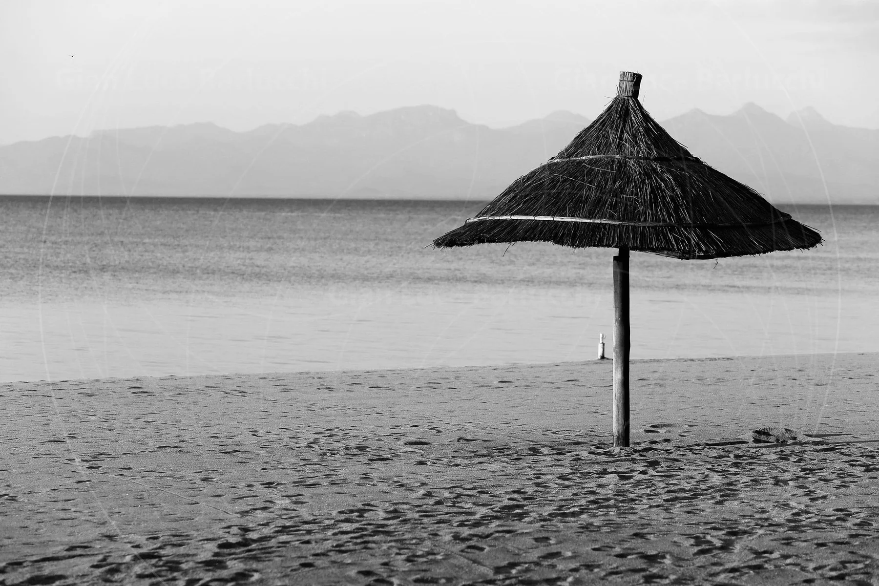 A thatched parasol on a quiet lakeside beach, photographed in black and white