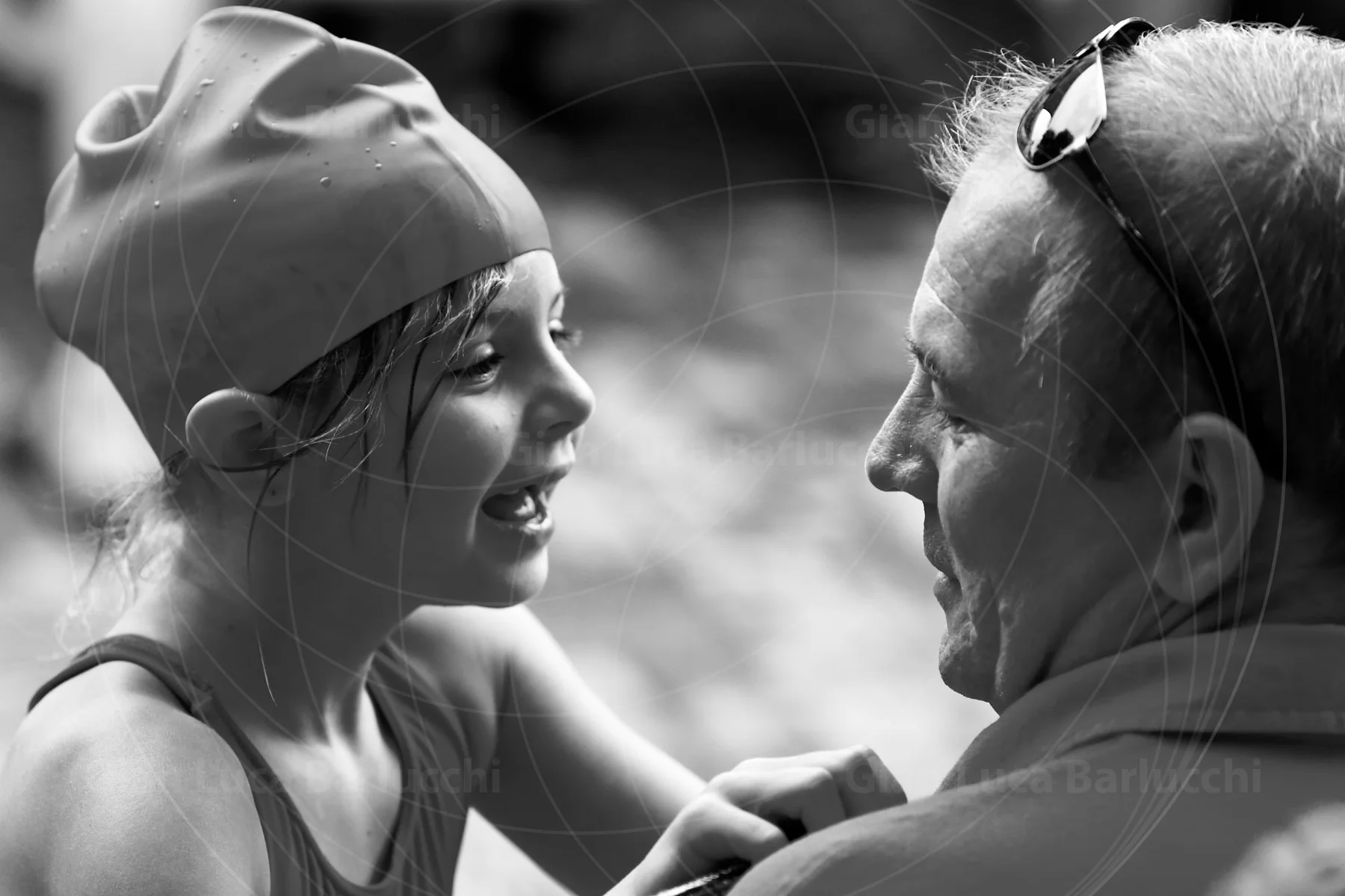 Black-and-white photograph of a child in a swimming cap smiling at an adult