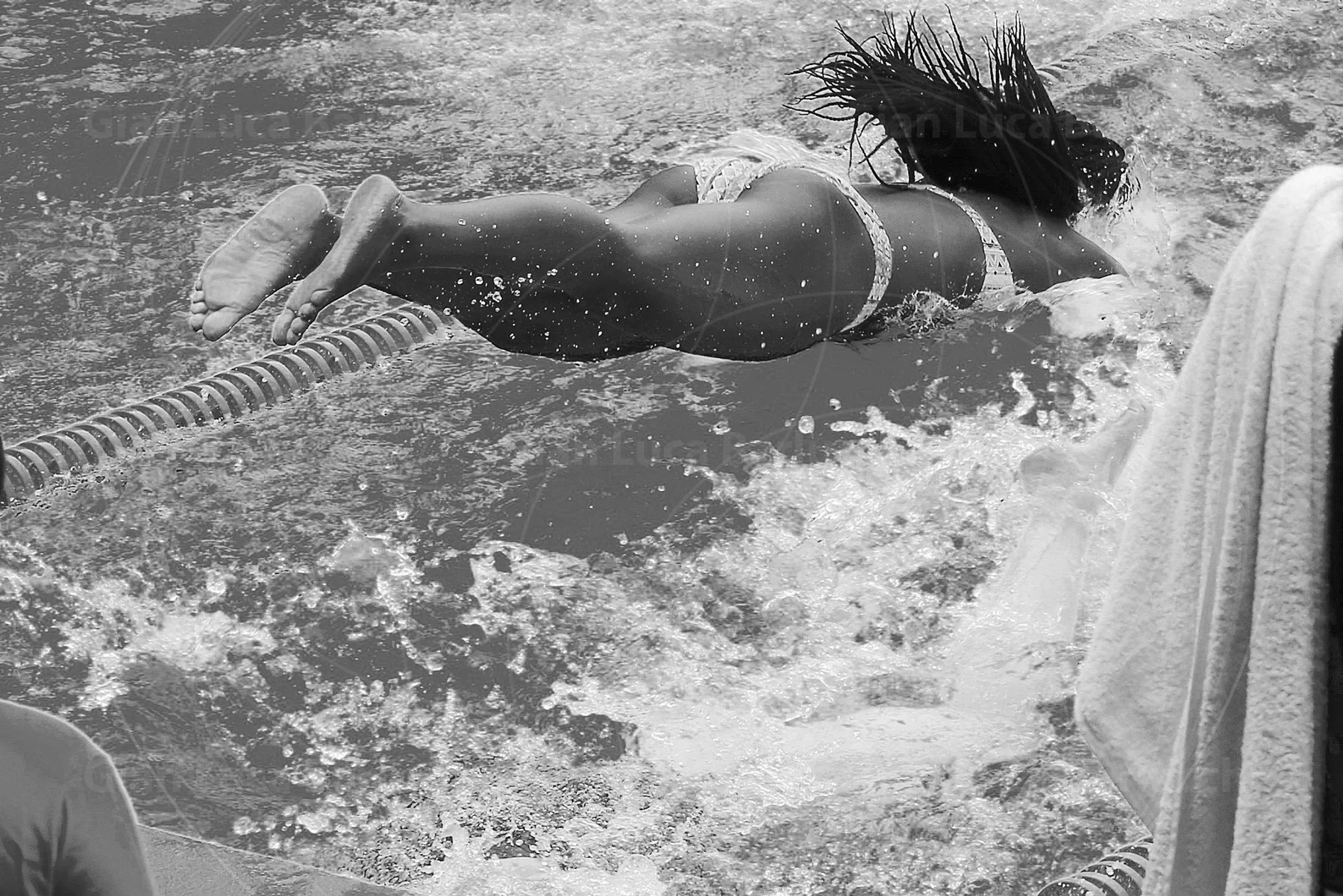 Black-and-white photograph of a swimmer diving over a lane rope into a pool