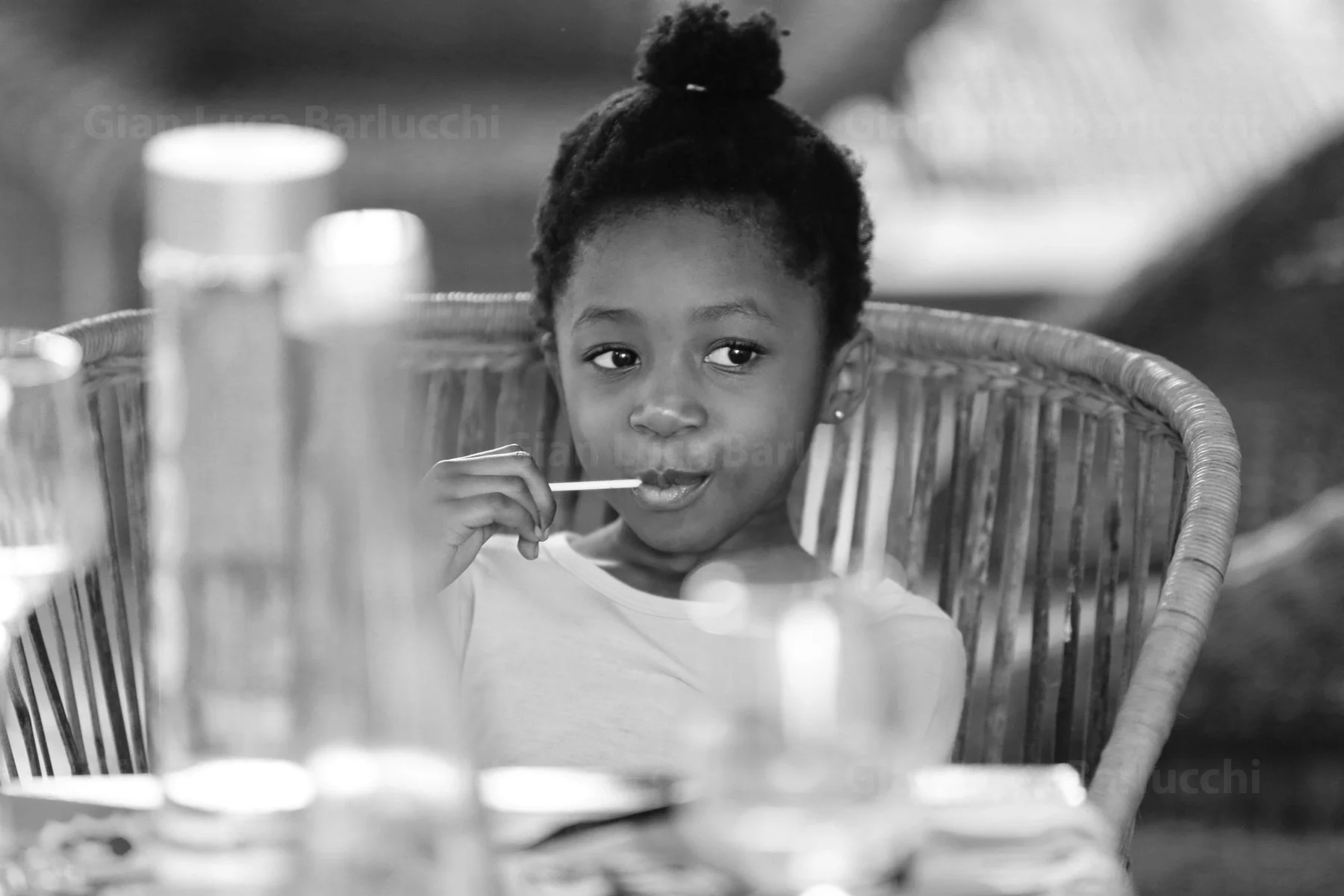 Black-and-white photograph of a child holding a lollipop at a table
