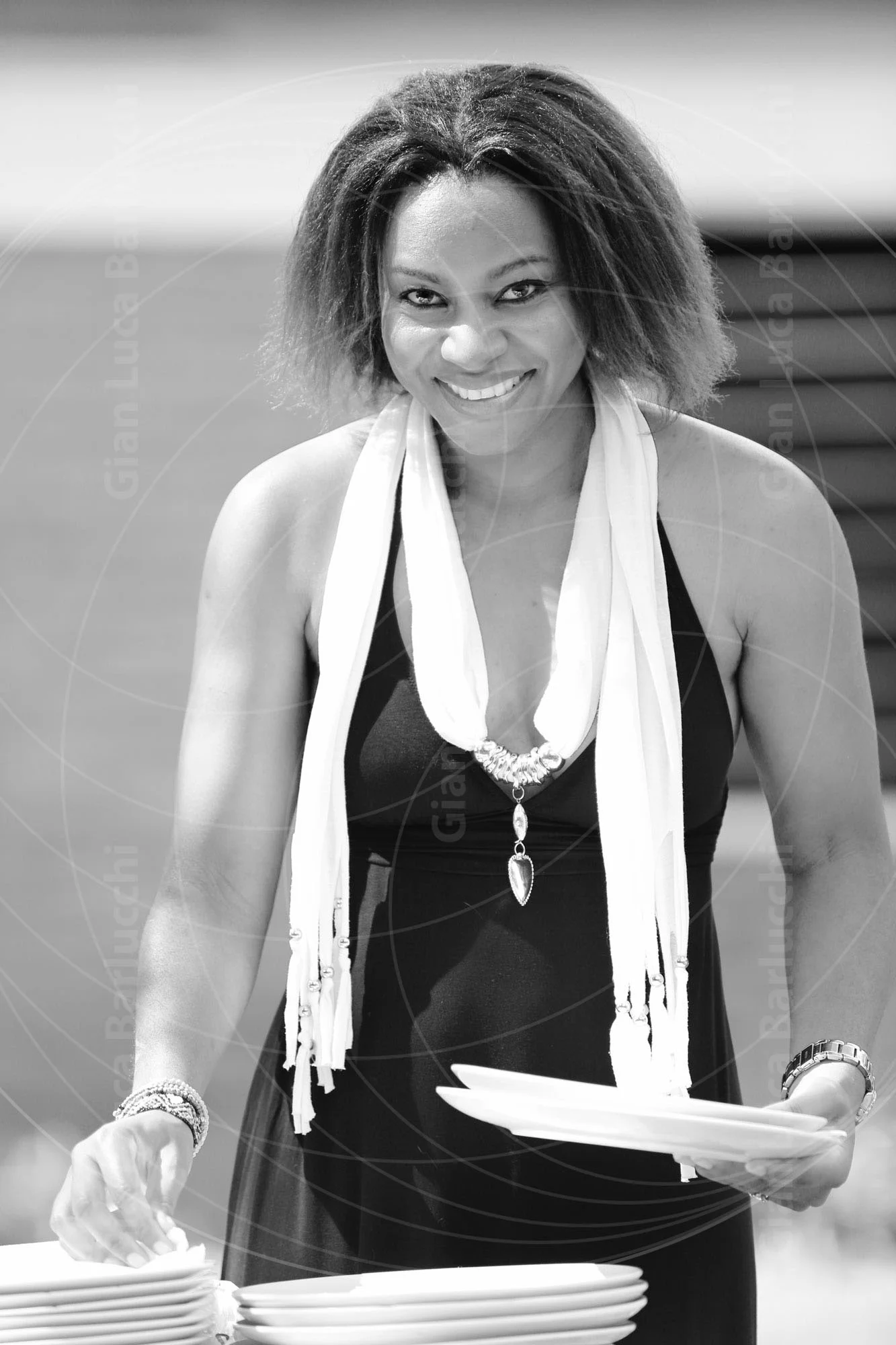 Black-and-white photograph of a smiling woman carrying a stack of plates