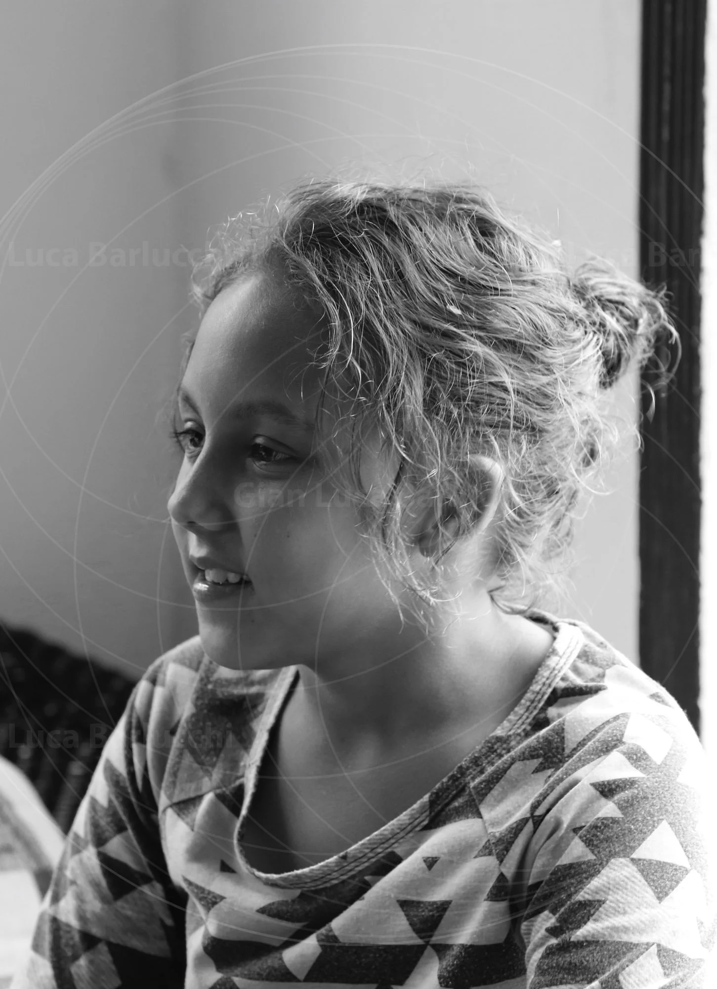 Black-and-white portrait of a curly-haired child seated beside a window