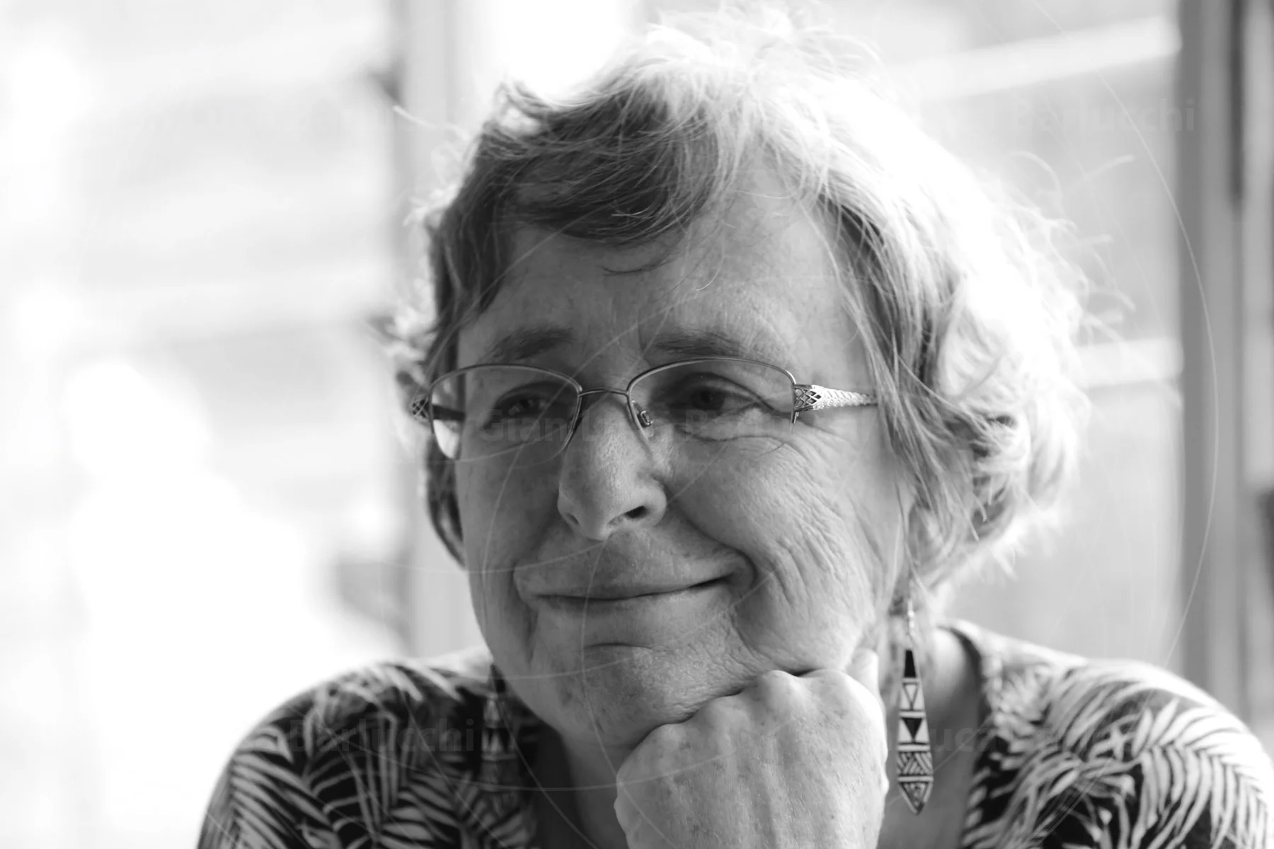 Black-and-white portrait of a smiling woman wearing glasses and resting her chin on her hand