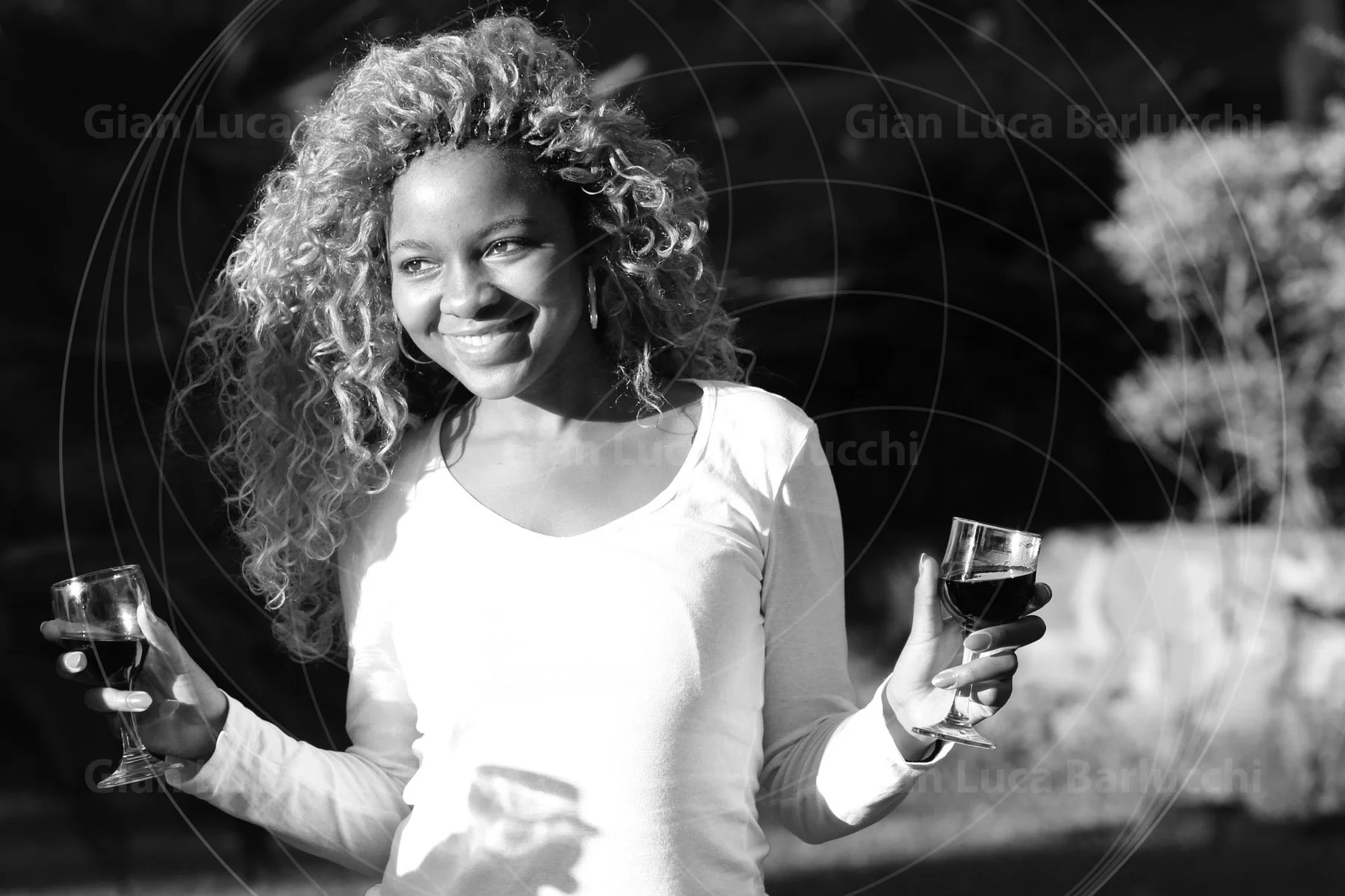 Black-and-white photograph of a smiling woman holding a glass in each hand