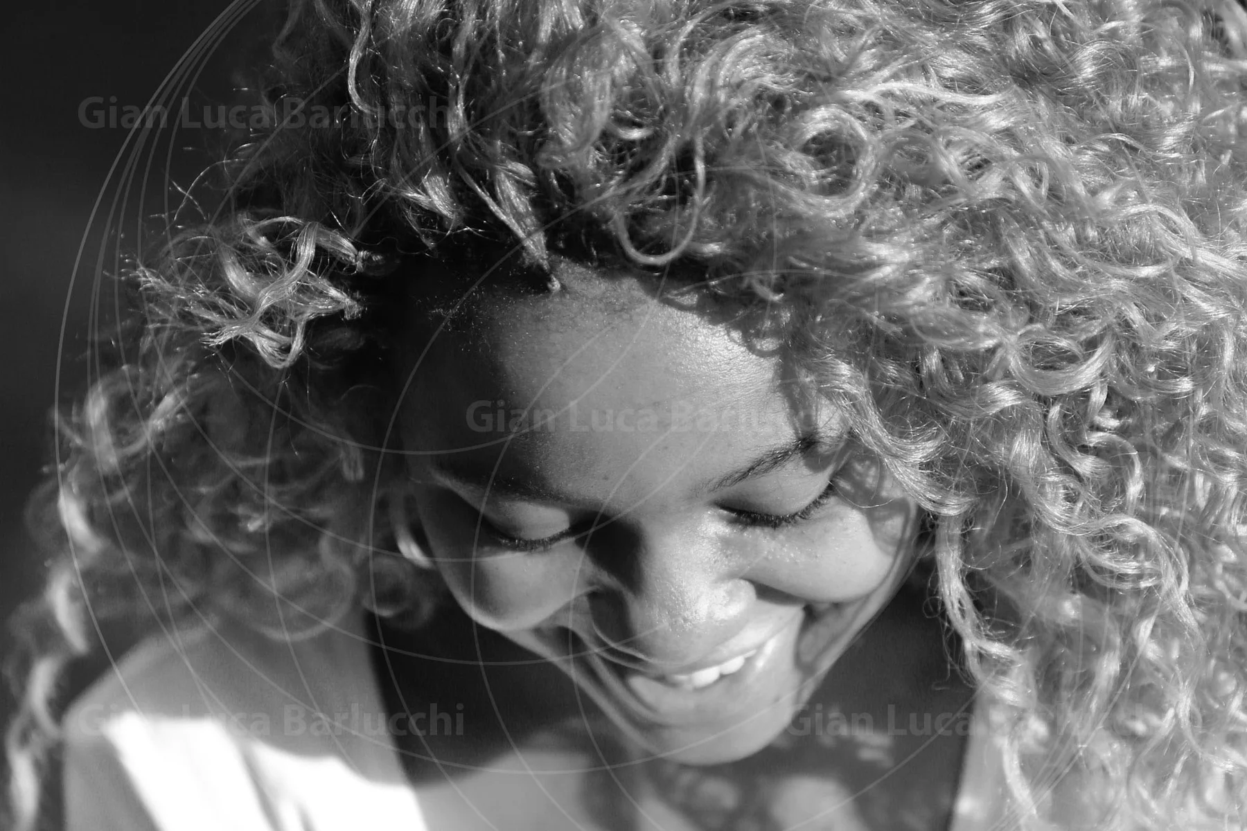 Black-and-white portrait of a curly-haired woman smiling with her head lowered