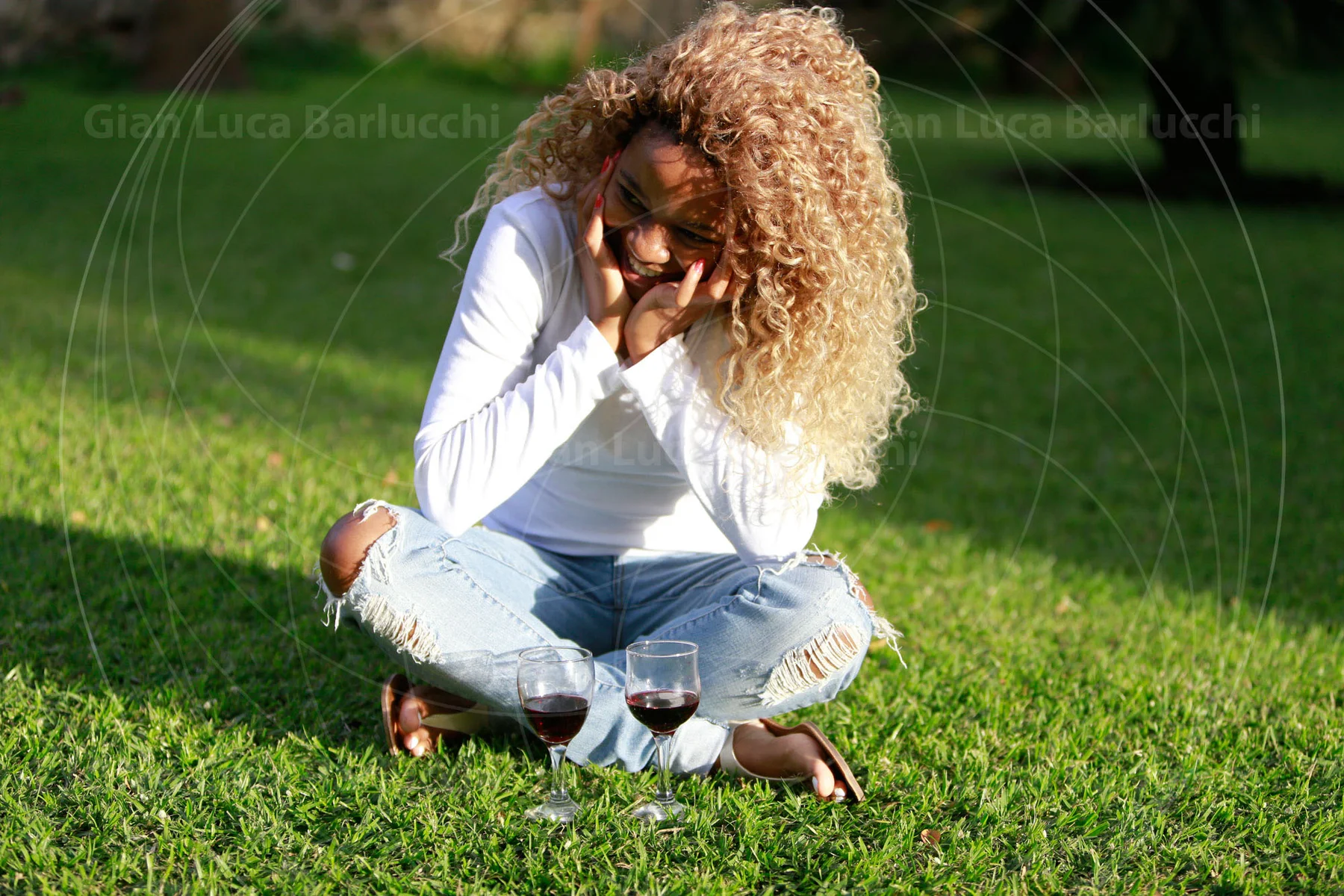 Woman sitting cross-legged on grass with her hands near her face