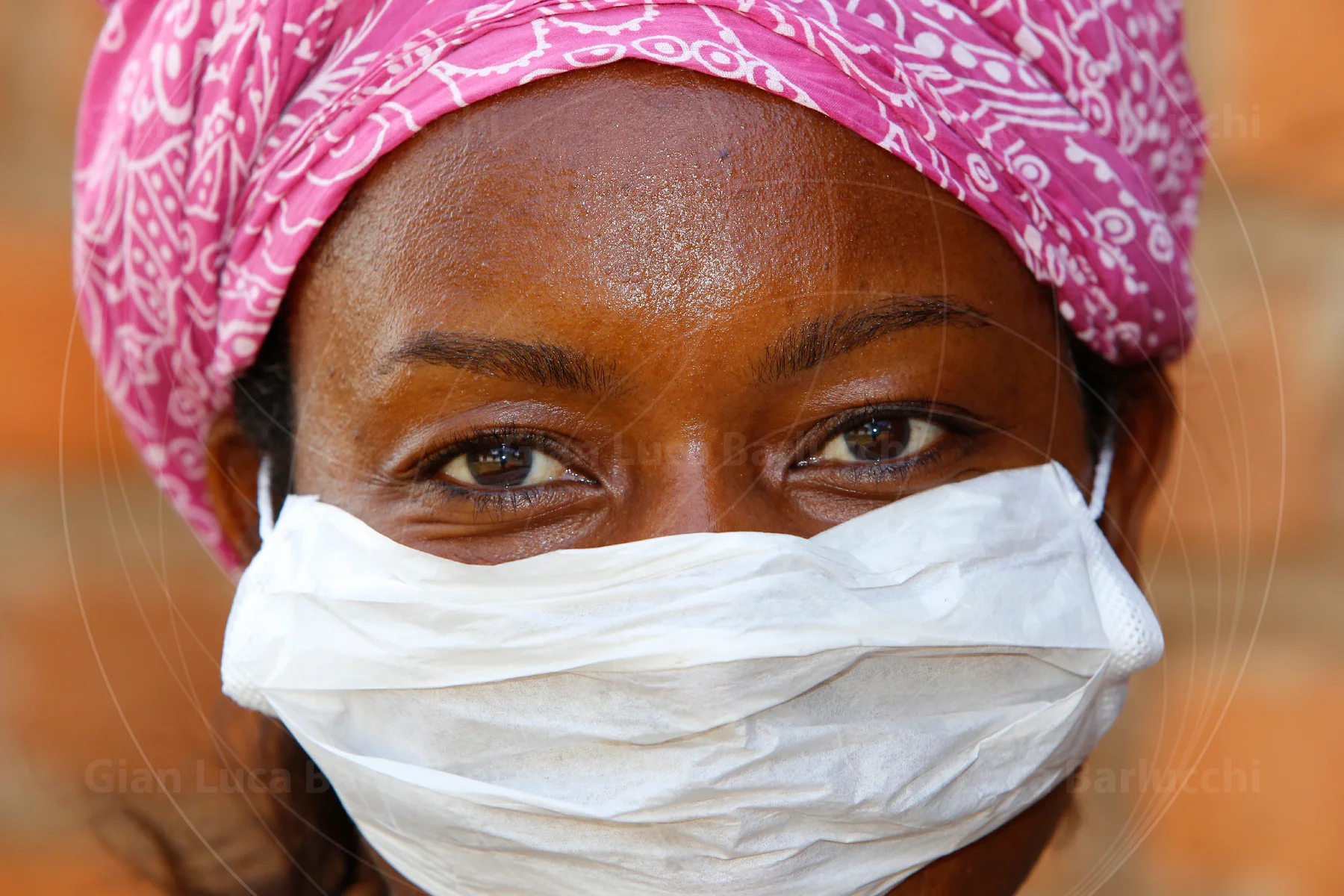Close-up of a woman wearing a pink headscarf and a white face mask