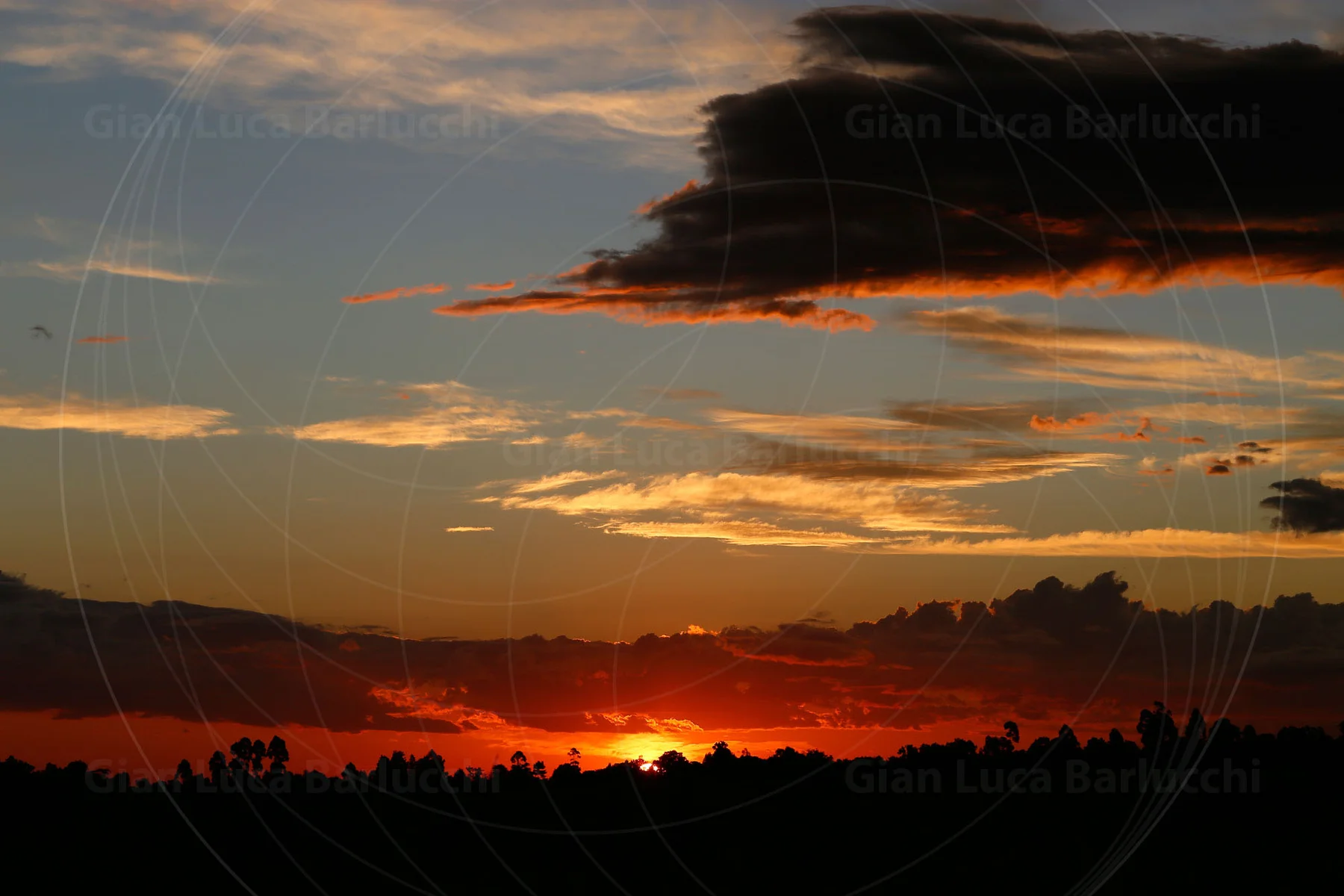 Orange sunset beneath a dark cloud bank over a silhouetted horizon