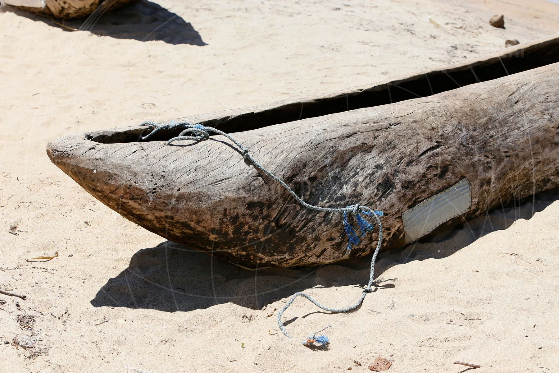 Weathered wooden canoe resting on pale sand with rope draped over its bow