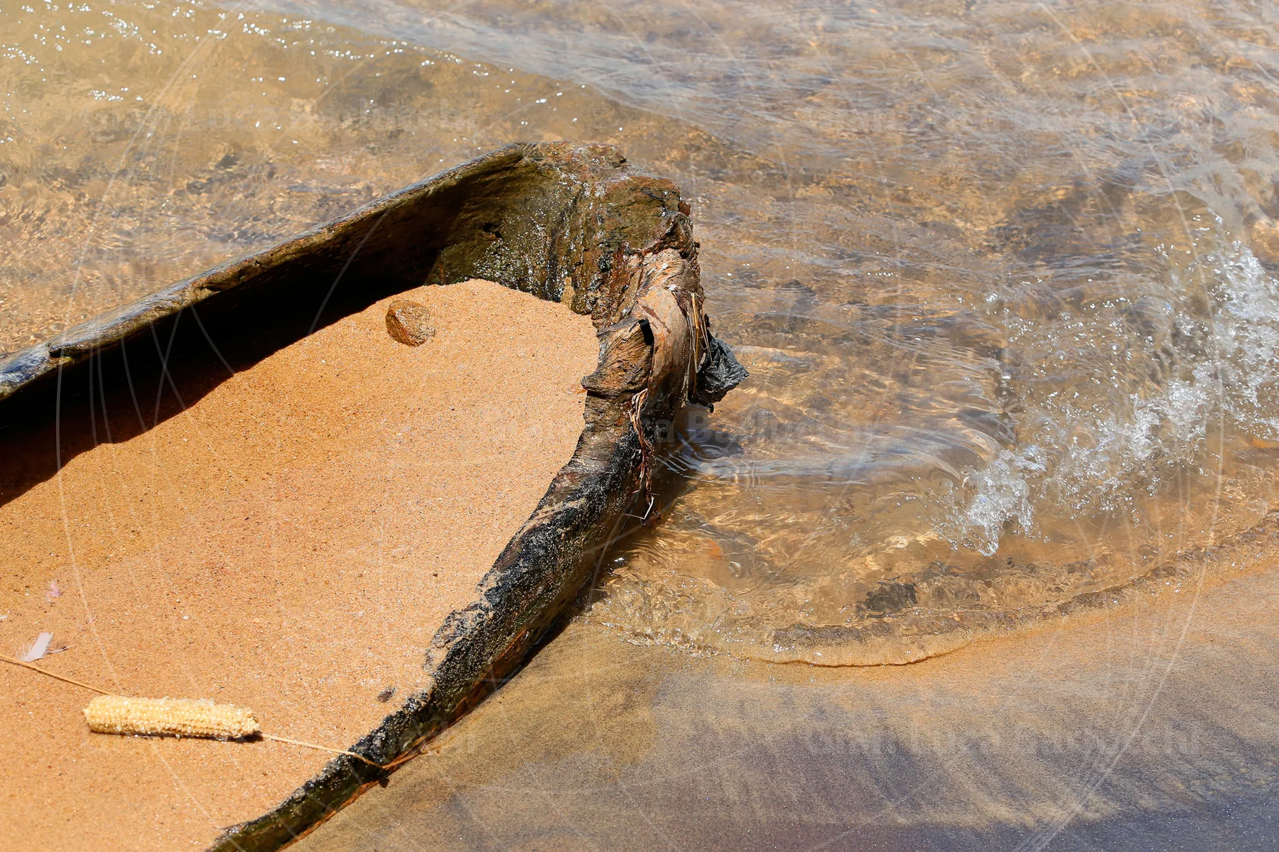 Water washing into the sand-filled bow of a wooden canoe