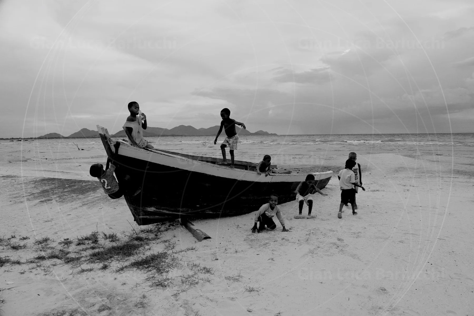 Black-and-white lakeside scene with children beside a wooden boat